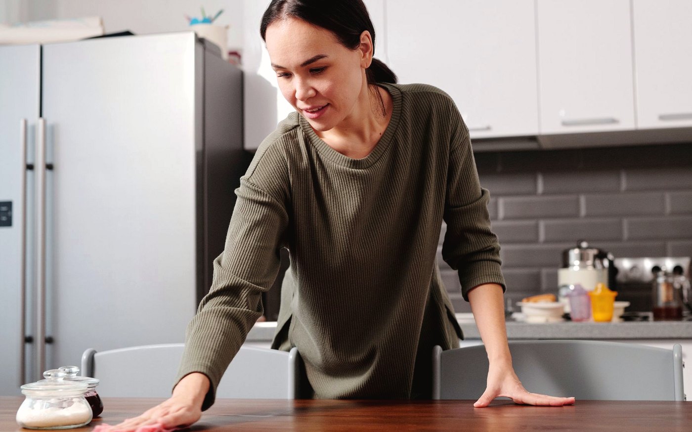 Woman wiping a wooden kitchen table in a domestic kitchen